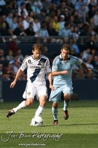 Sporting_KC_vs_LA_Galaxy_4-7-12_1180 LA Galaxy Midfielder Mike Magee (#18) kicks the ball as Sporting Kansas City Midfielder Graham Zusi (#8) approaches at LIVESTRONG Sporting Park in Kansas City, Kansas on April 7, 2012. (Photo: Joey Bahr, www.joeybahr.com)
